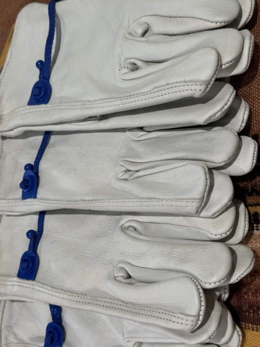 Stack of white leather gloves with blue buttons on a brown surface