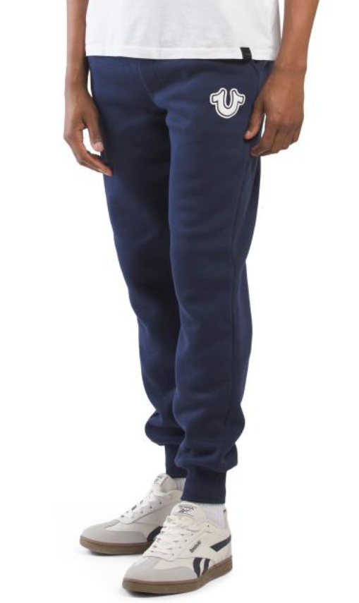 Navy blue jogger pants with a logo on the chest worn by a person on a white background