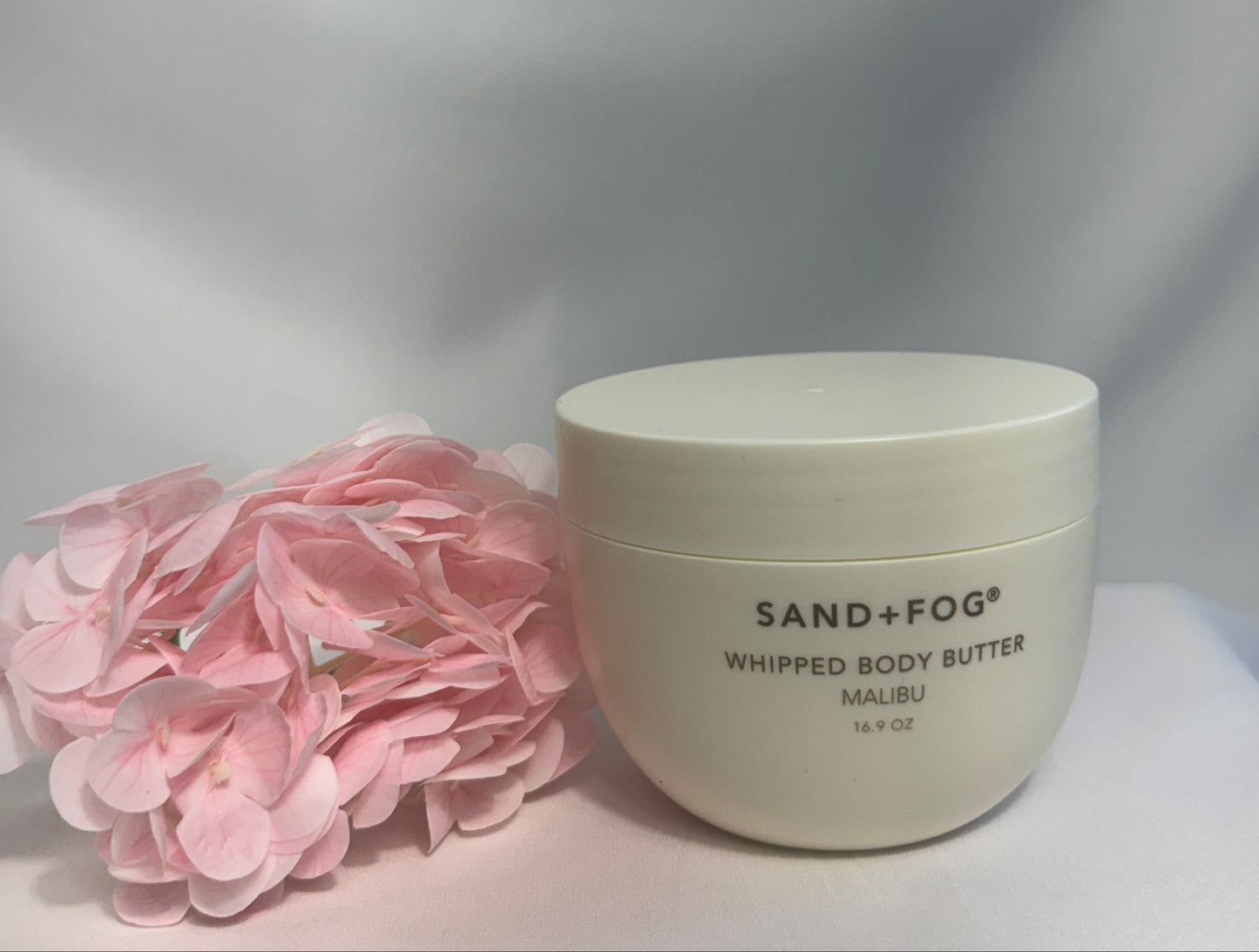 Whipped body butter with pink flowers on a light gray background