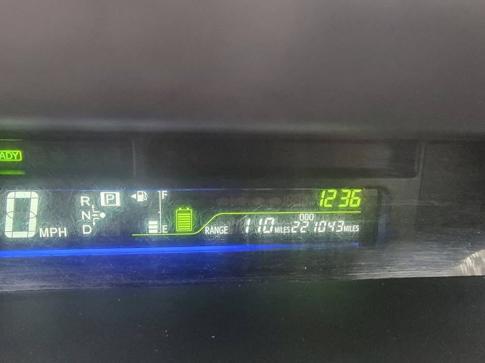 Digital dashboard display of a 2015 Toyota Prius v showing 210,043 miles on the odometer, full battery level, and 110-mile fuel range
