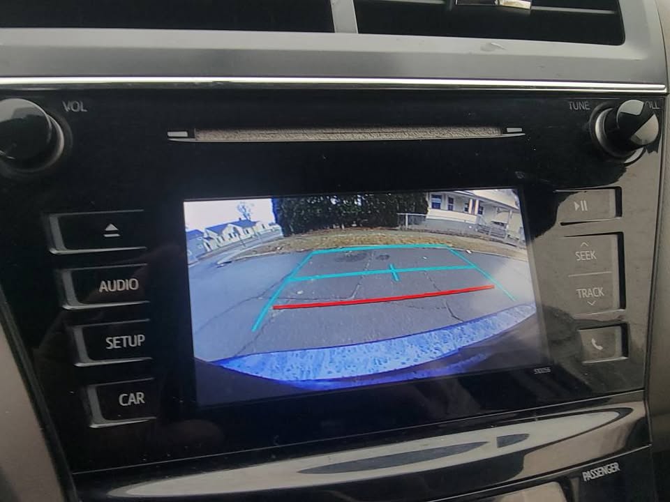 2015 Toyota Prius v backup camera display with colored parking guidelines, showing rear street view with curb and surrounding neighborhood homes