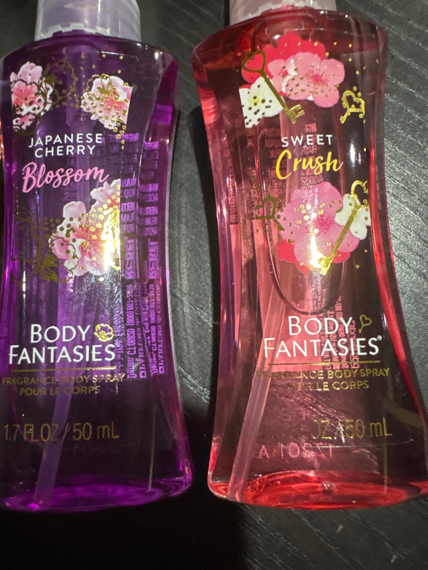 Two bottles of Body Fantasies body wash with cherry blossom design on a reflective surface.