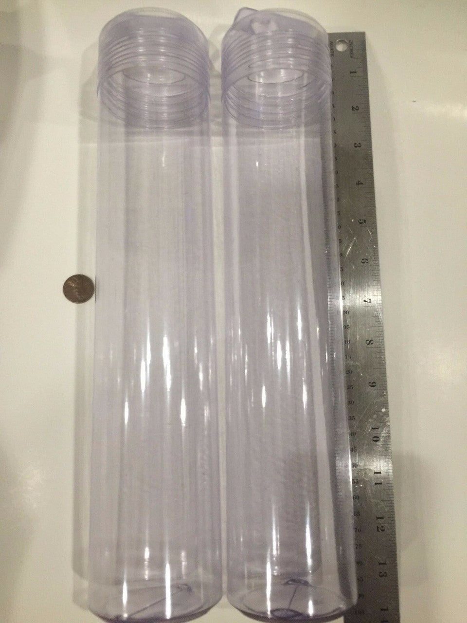Two clear plastic tubes with caps on a metallic surface with a ruler.