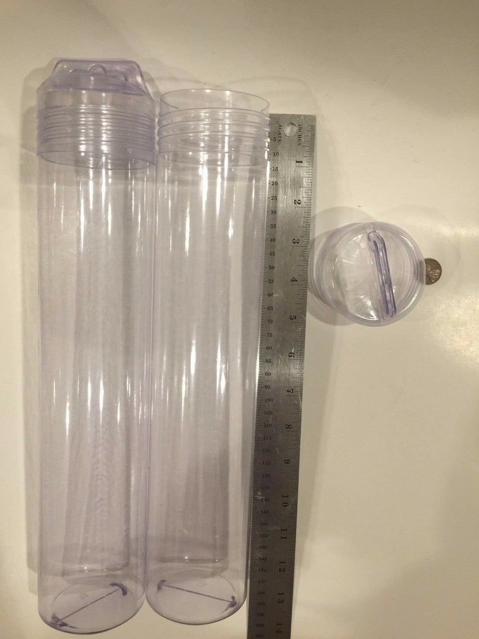 Clear plastic tubes with lids on a light-colored surface, with a ruler for scale.