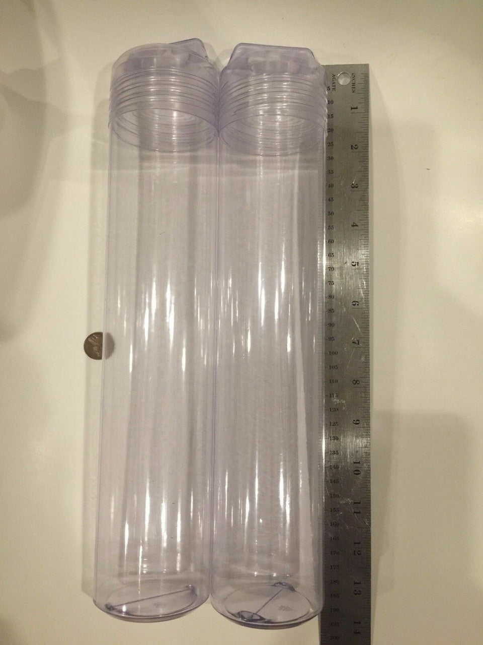 Two long clear plastic tubes with a ruler beside them on a plain background.