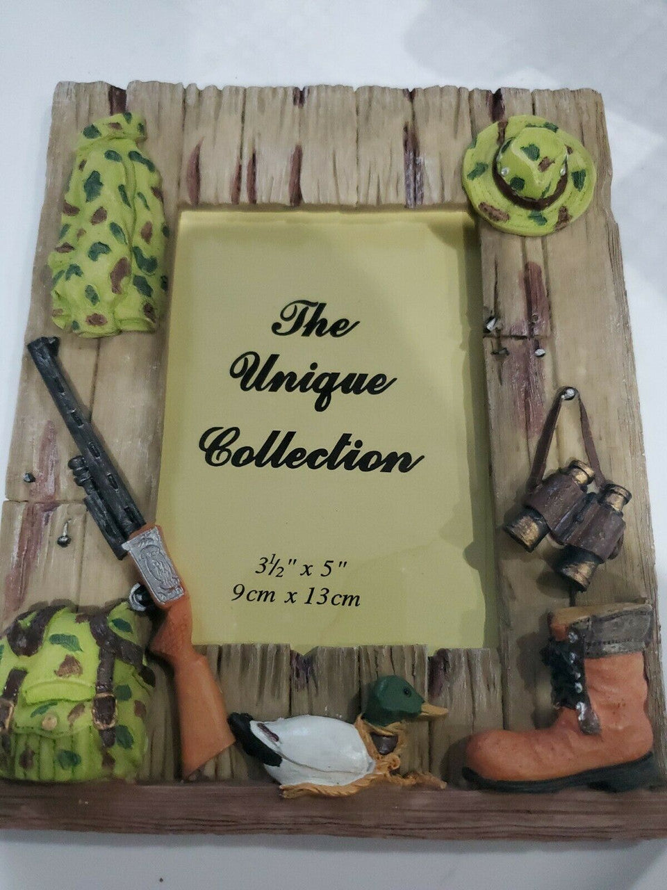 A decorative photo frame with a hunting theme, including a depiction of boots, camouflage clothing, and a gun, surrounded by a wooden border.
