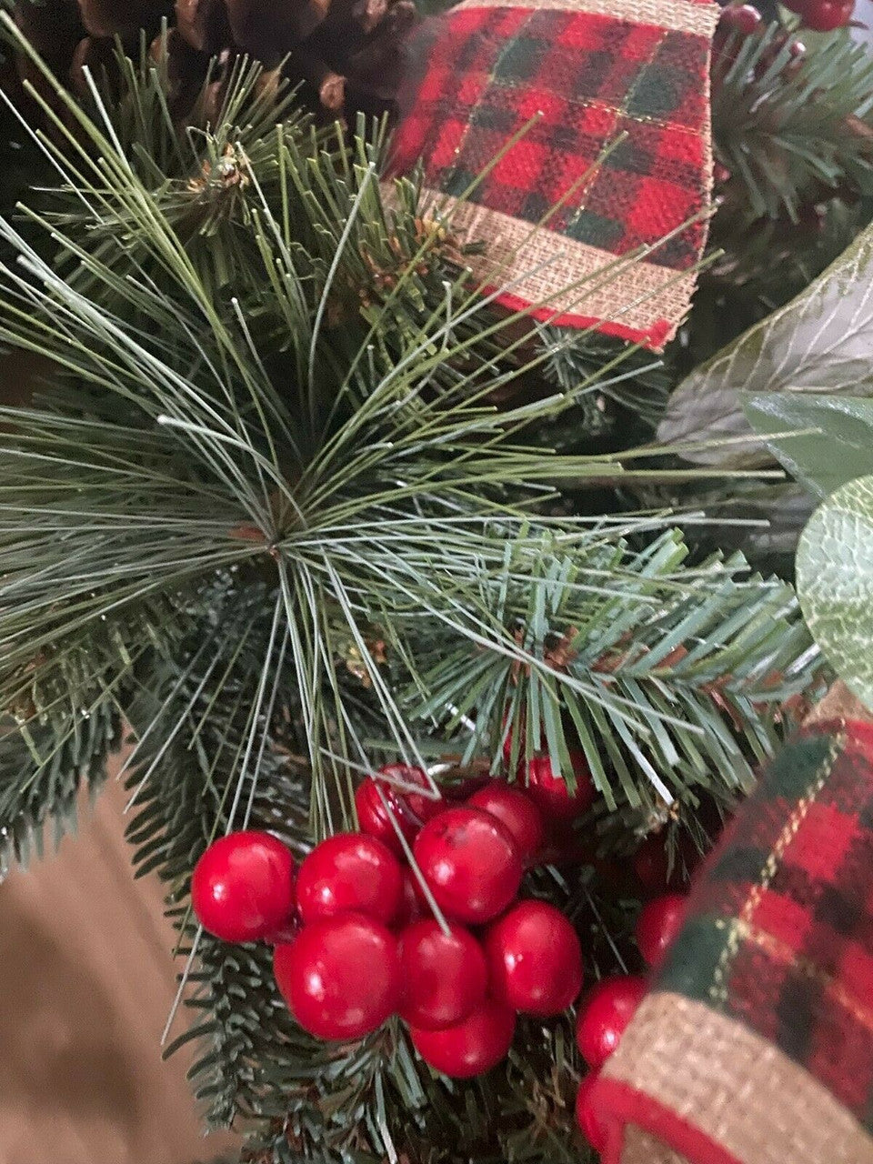 Close-up of a Christmas tree with red berries and plaid ribbon.