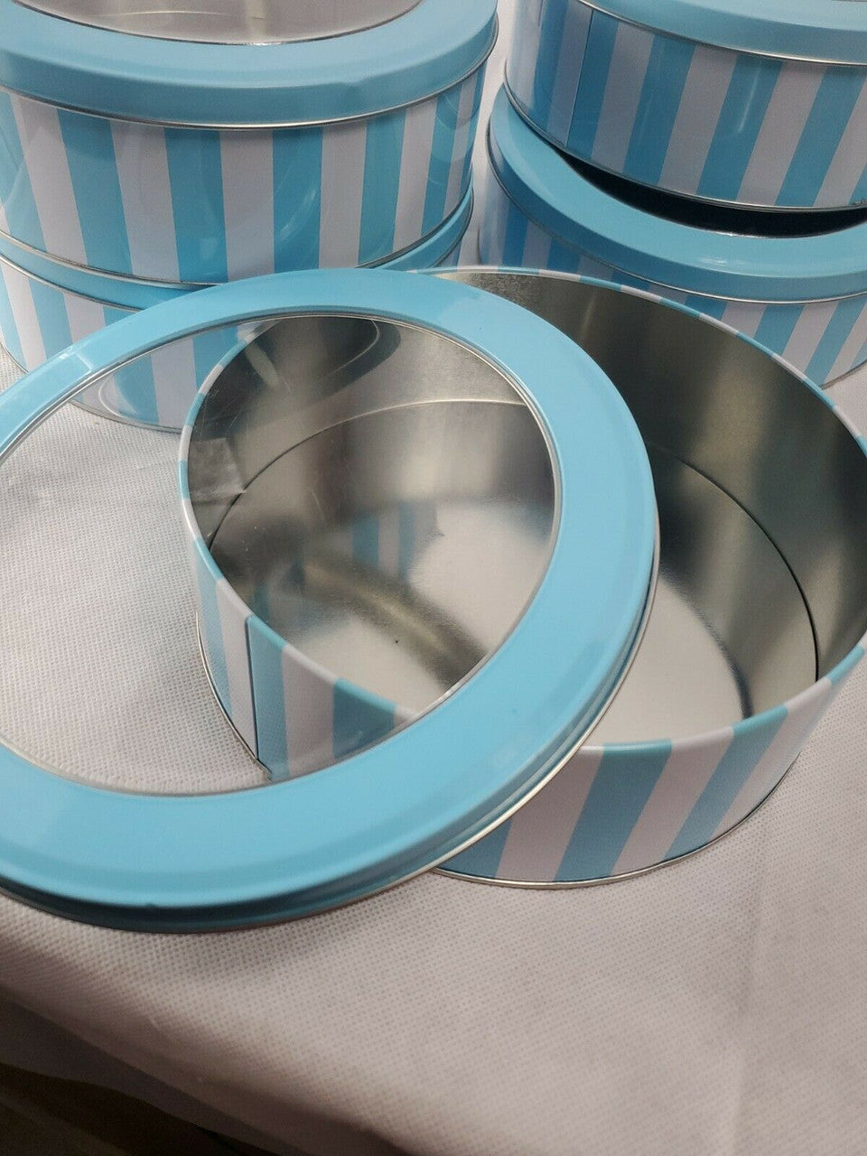 Stack of metal containers with blue striped lids on a gray surface.