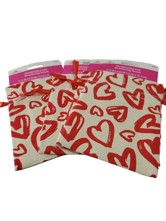 Burlap drawstring gift bags with a pattern of red hearts, tied with a ribbon.