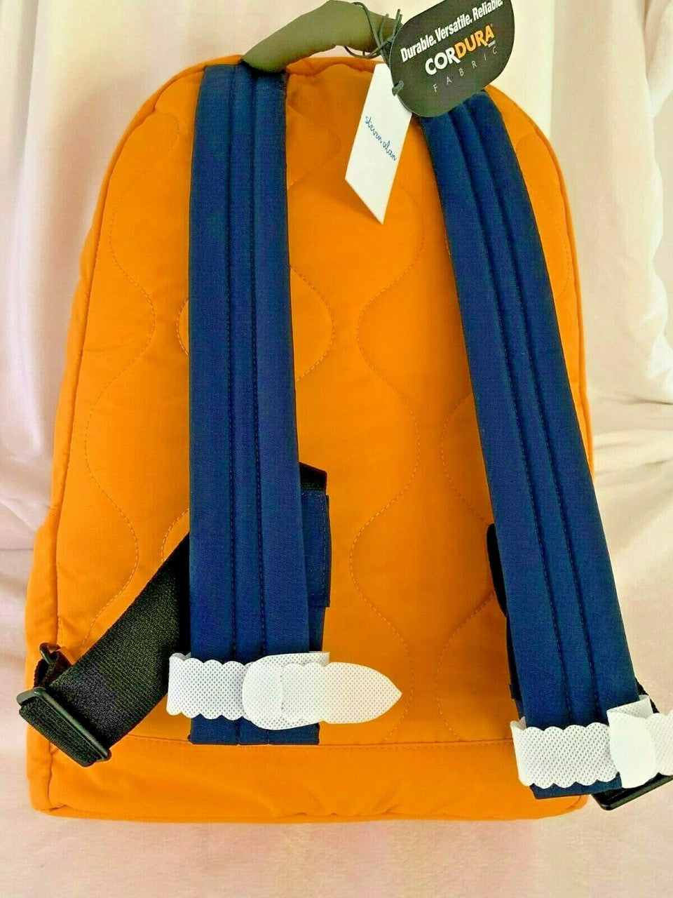 Orange backpack with blue straps and a tag on a light pink background.