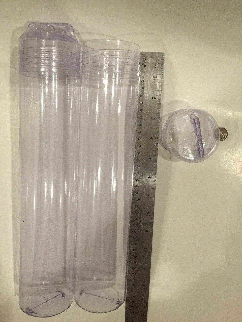 Two clear plastic tubes with a ruler for scale on a plain background.