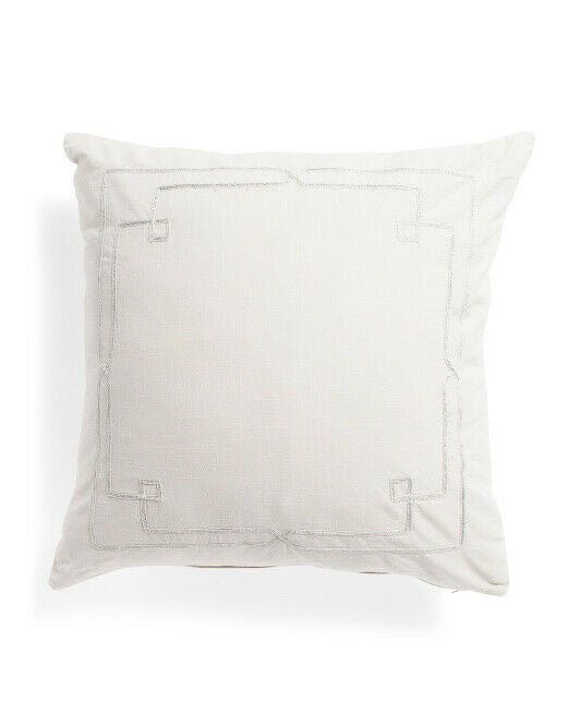 A white linen look decorative pillow with metallic embroidery and a visible zipper edge.