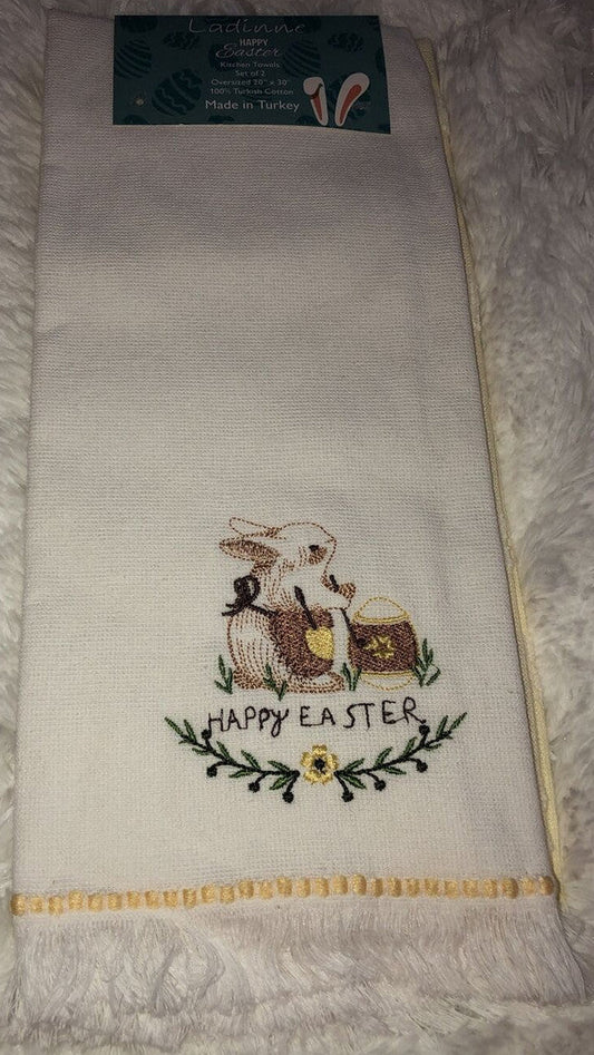 A set of two kitchen towels with a white background featuring embroidered white bunnies and the text 'HAPPY EASTER' on one of the towels.