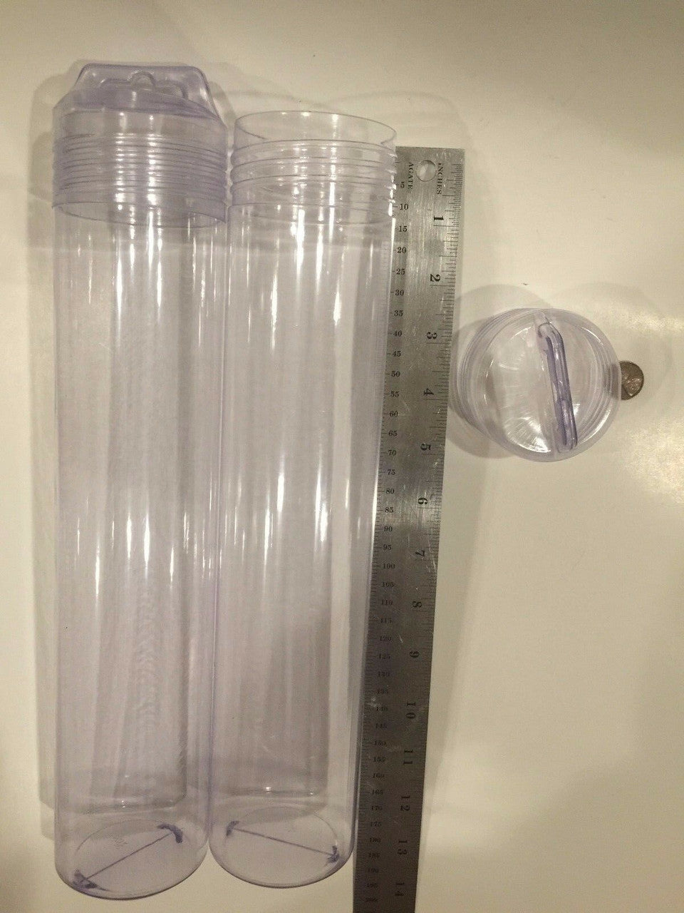 Six clear plastic tubes with hang caps displayed next to a ruler for scale.