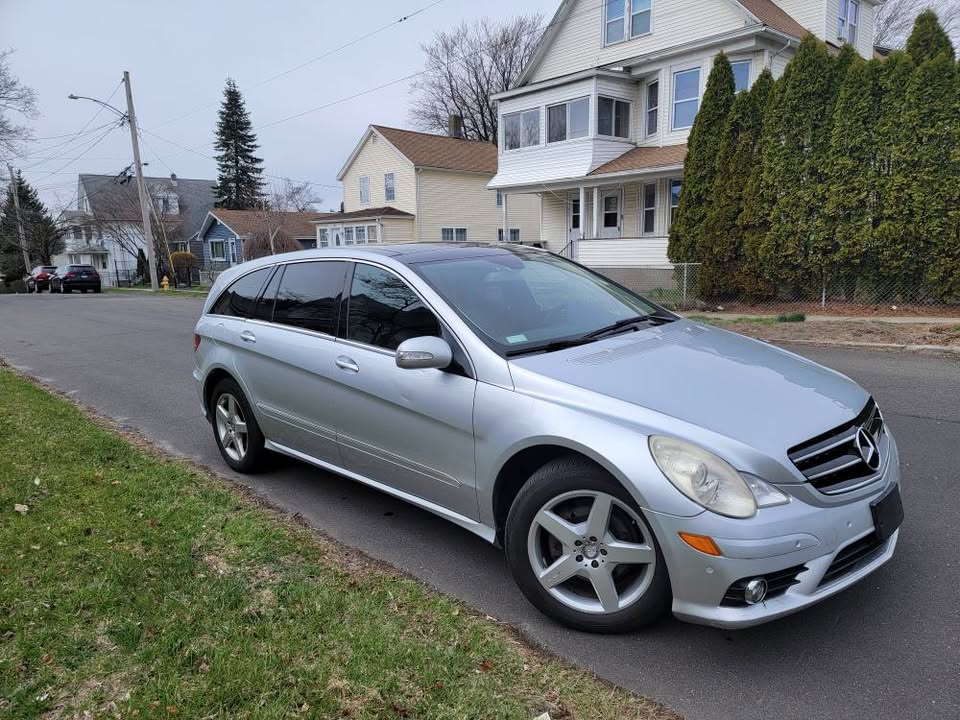 Front passenger-side angle of silver 2009 Mercedes-Benz R350 AWD parked on residential street, showing grille, headlights, and alloy wheels