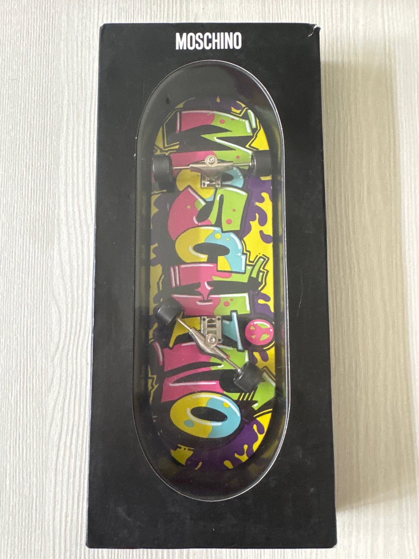 Colorful MOSCHINO printed iPhone 6 case displayed vertically, shaped like a skateboard, boxed
