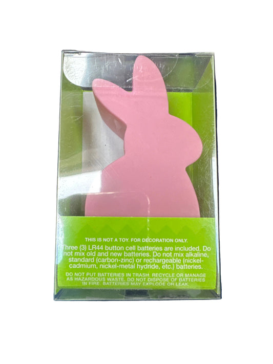 Pink bunny-shaped object in clear packaging with green label on a dark background