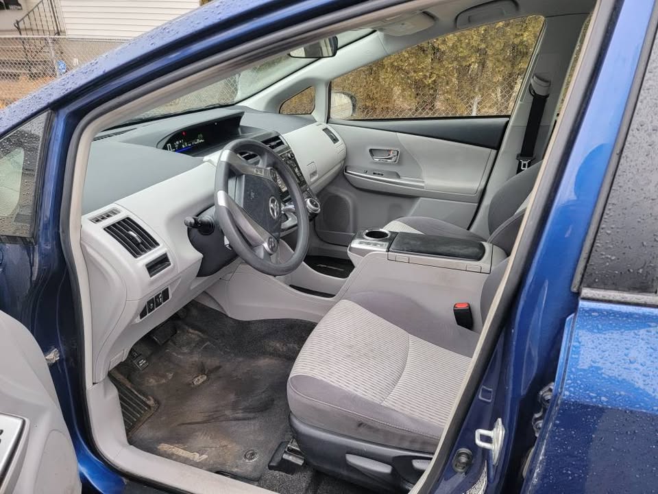 Driver-side view of the interior of a blue 2015 Toyota Prius v, showing the dashboard, steering wheel, front seats, and center console