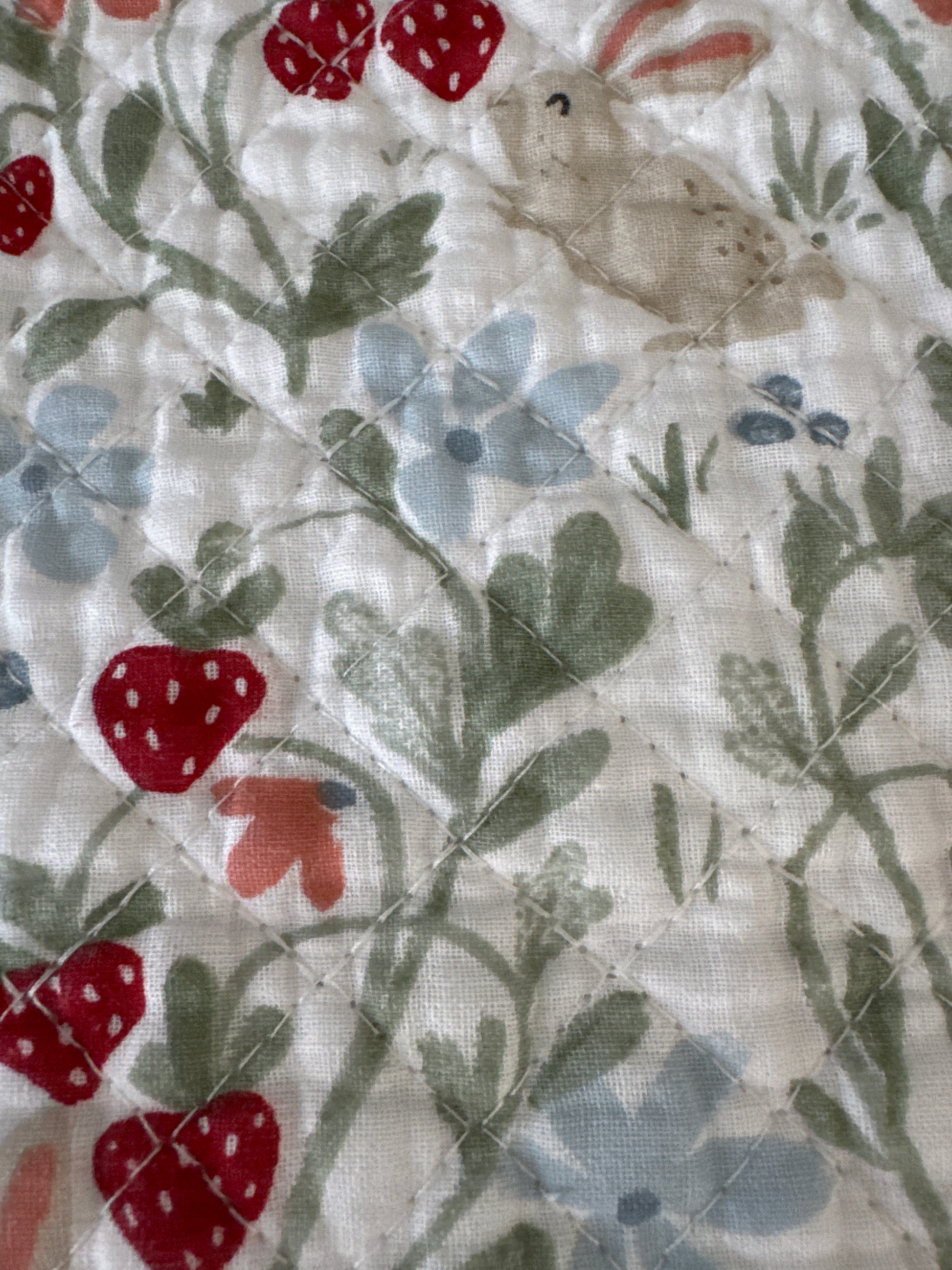 Close-up of a placemat with a design featuring a bunny and strawberries, with a quilted pattern visible on the fabric