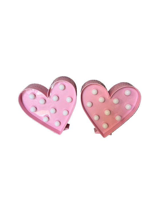Two pink heart-shaped clips with white polka dots on a striped fabric background
