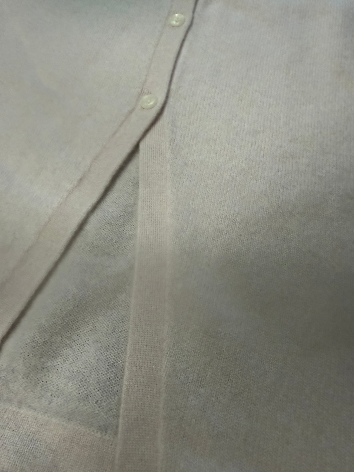 Close-up of a light beige or off-white knit fabric garment, showing a folded corner with two small buttons and a ribbed trim.