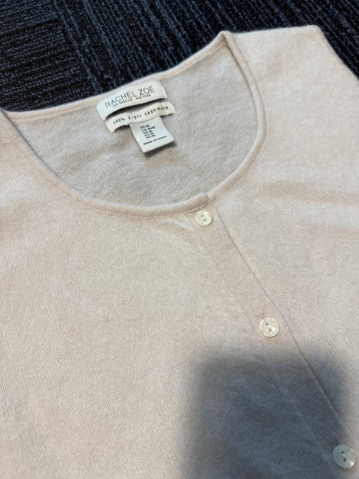 A close-up of a light beige knit top by Rachel Zoe, featuring a crew neck, and a visible brand label.