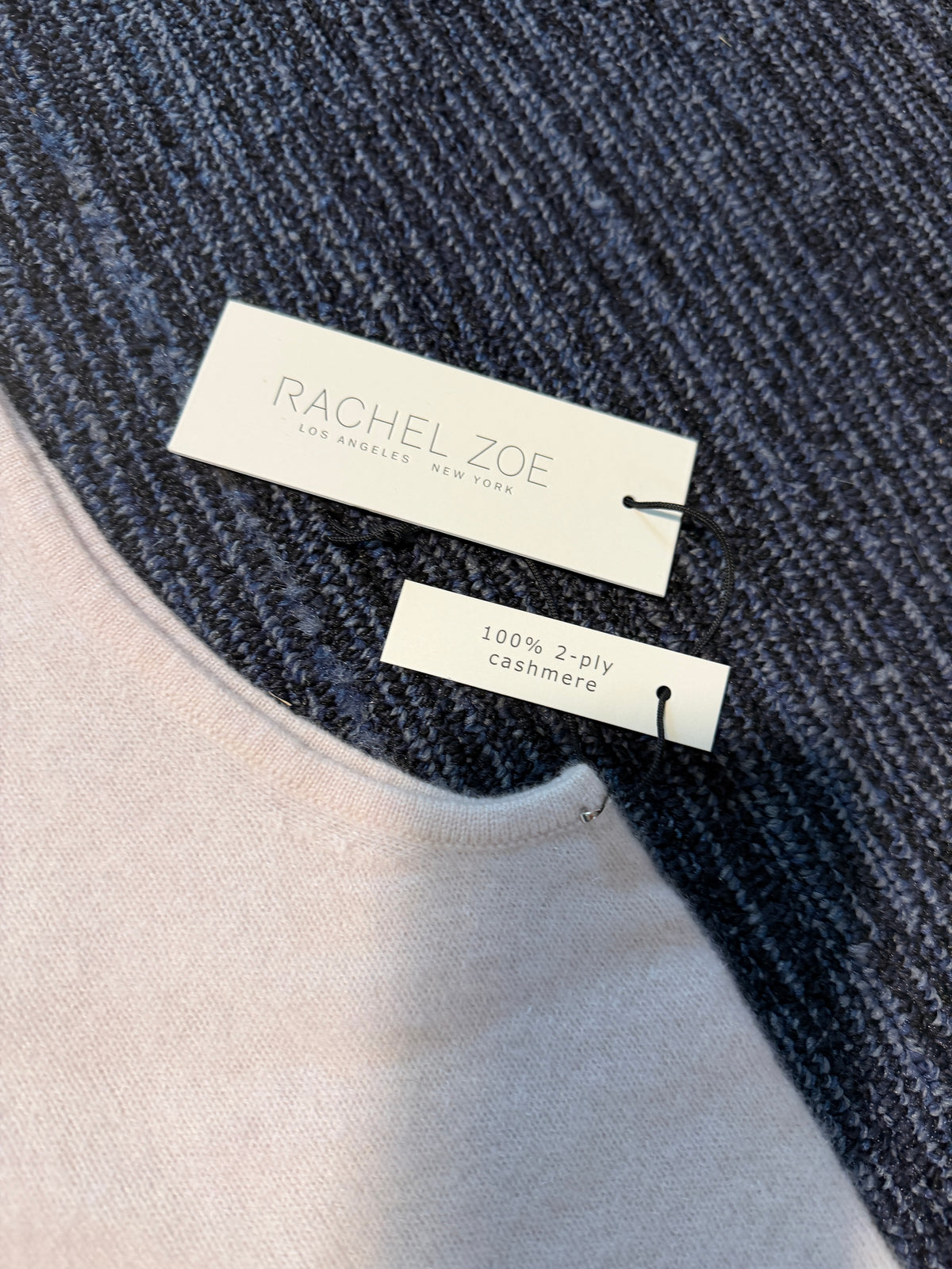 Close-up of a Rachel Zoe sweater showing a navy blue textured knit layer over a light blush pink cashmere layer, with two brand tags attached.