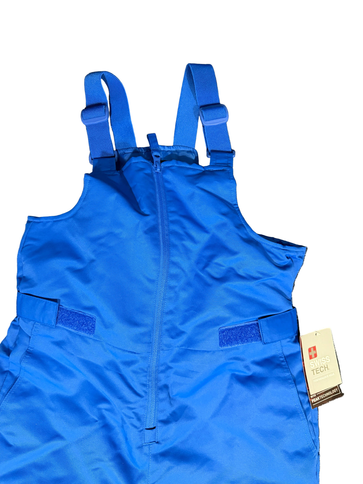 A bright blue snow bib laid flat , featuring a front zipper, adjustable shoulder straps, side pockets with velcro closures, and a hangtag attached.