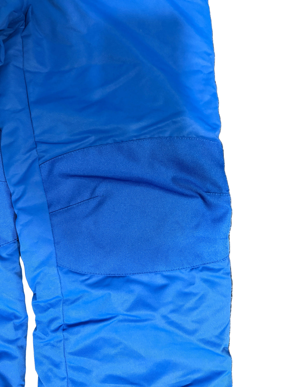 A close-up of bright blue insulated pants laid flat , showing the fabric texture and a large patch material on the leg.