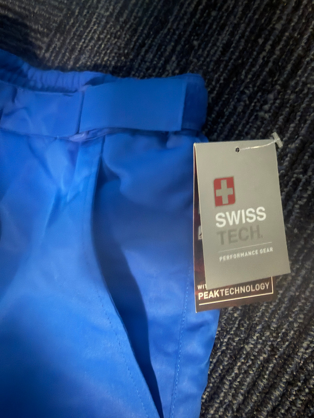 Close-up of bright blue pants with a hangtag reading SWISS TECH. and PEAKTECHNOLOGY