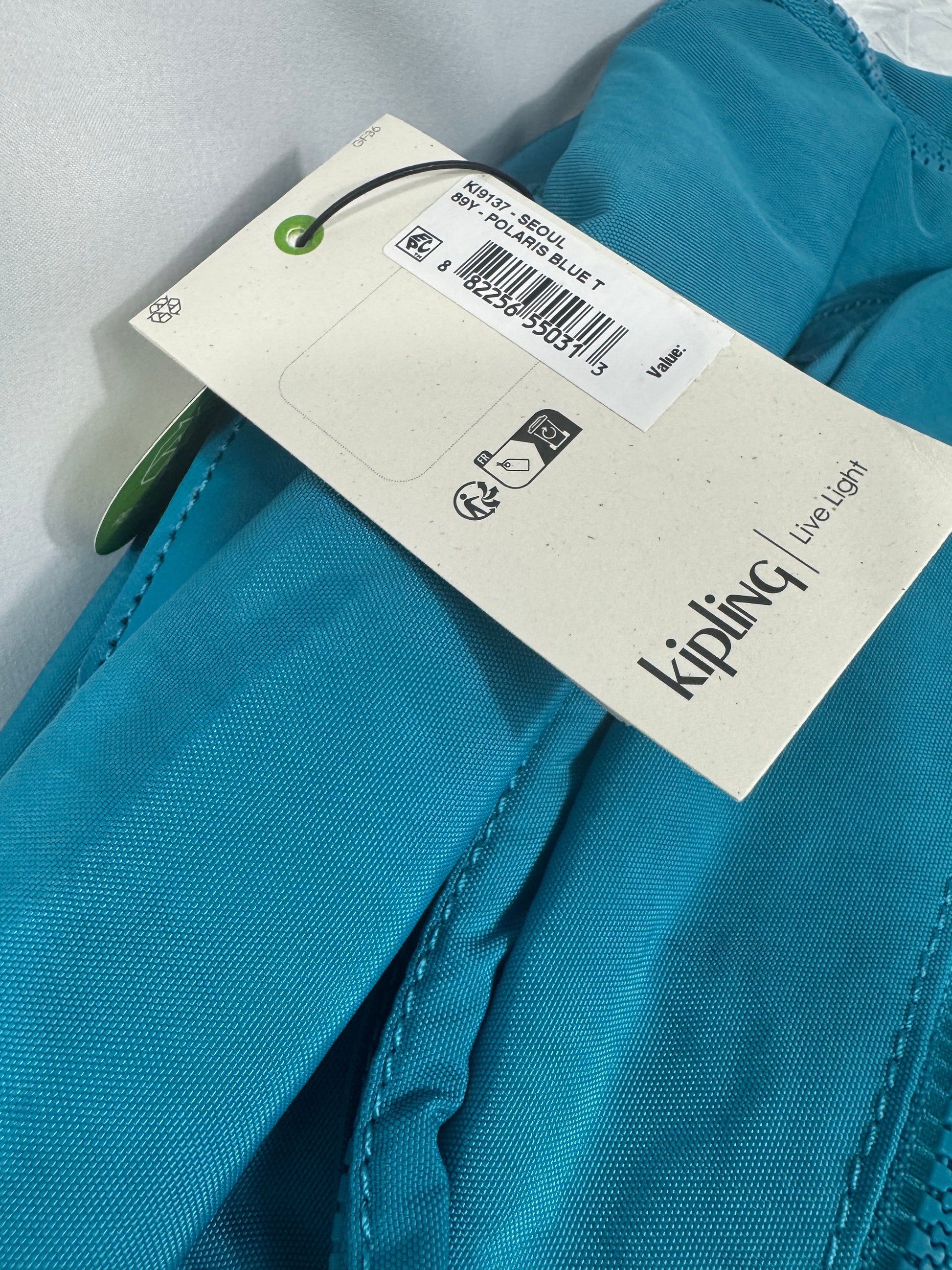 Close-up of a turquoise garment with a Kipling tag on a light gray background