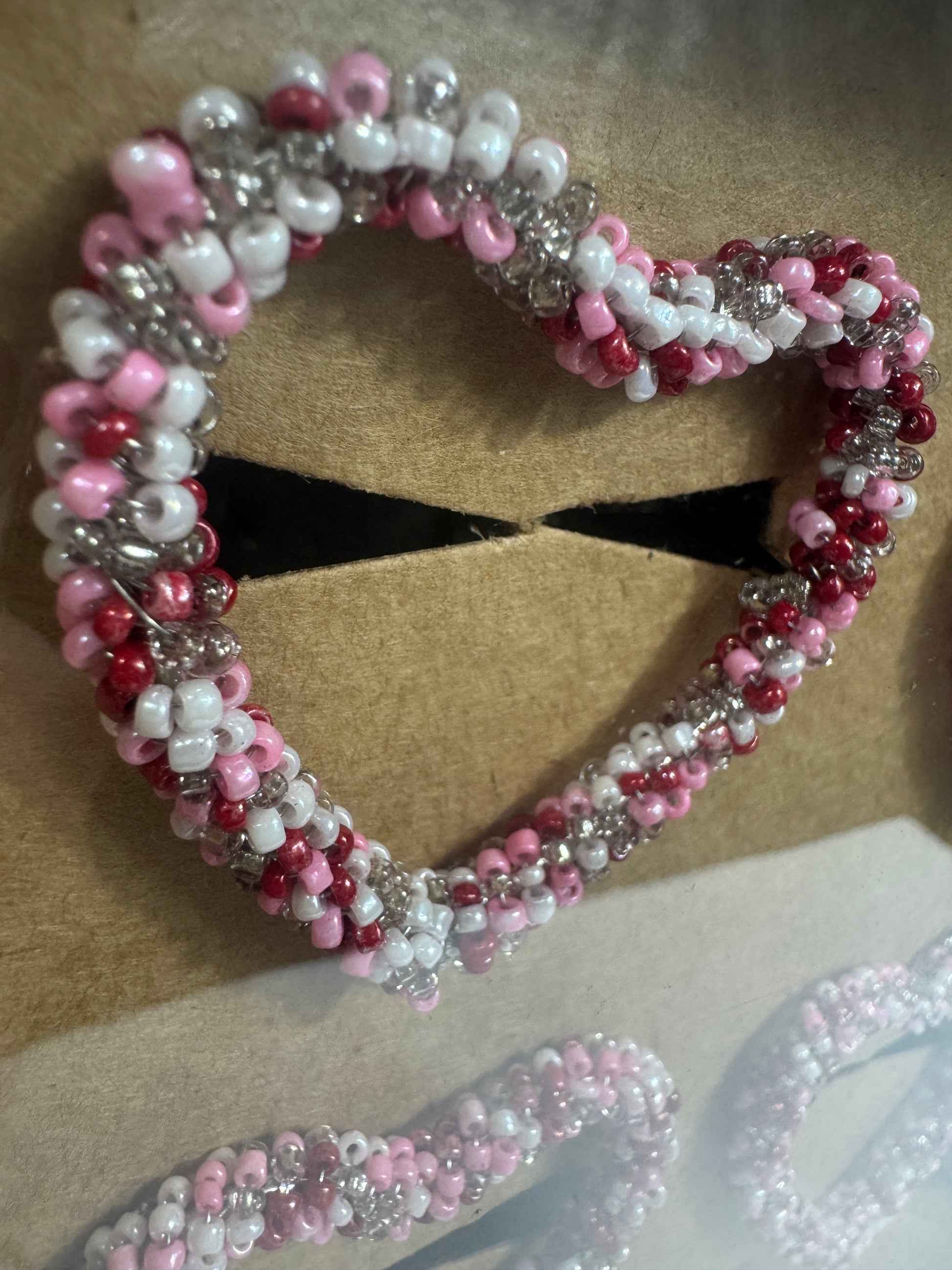Beaded heart shaped napking rings with pink, white, and red beads on a beige background
