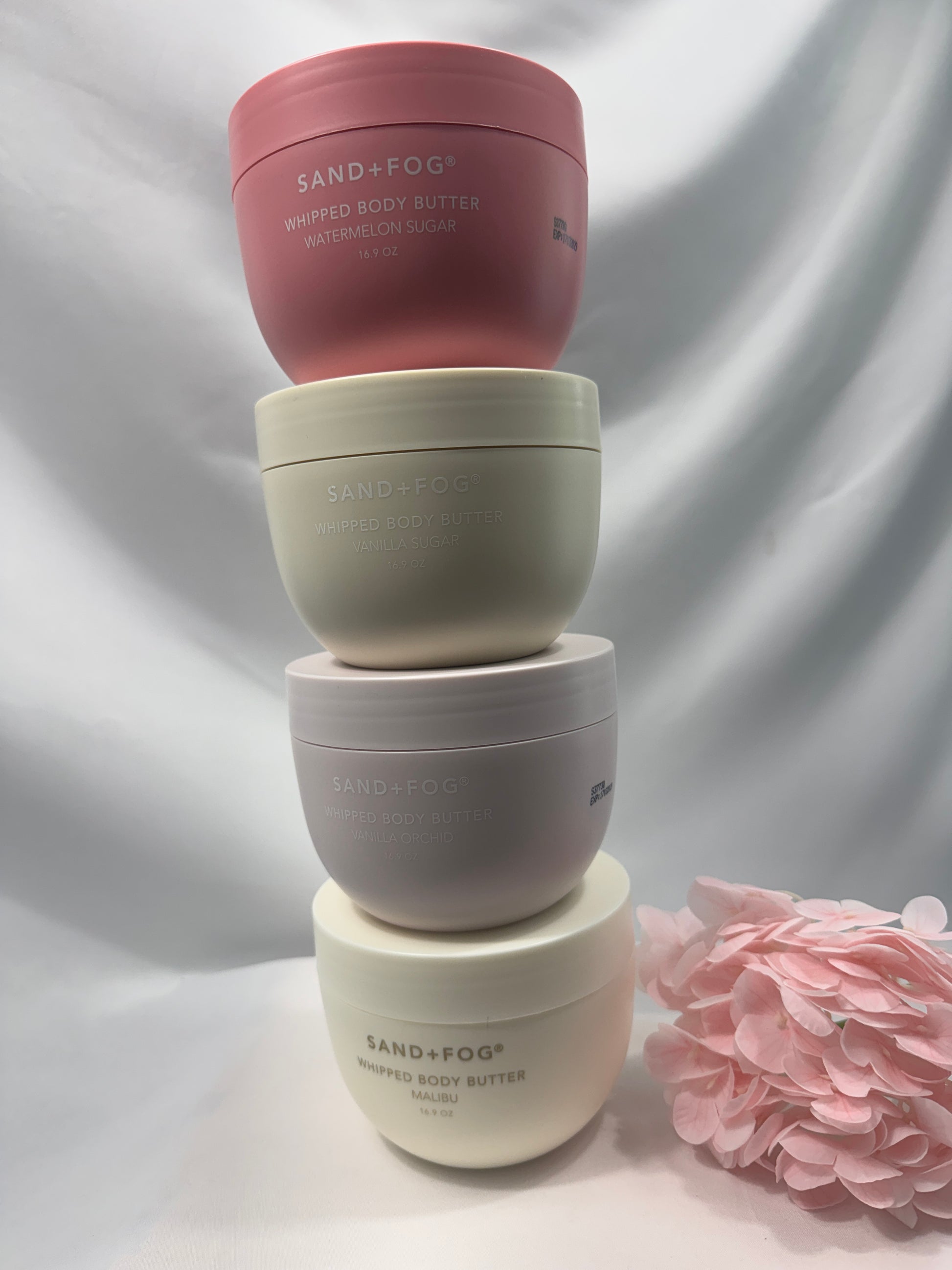 Four skincare bottles of different sizes on a soft, blurred background with a pink flower.