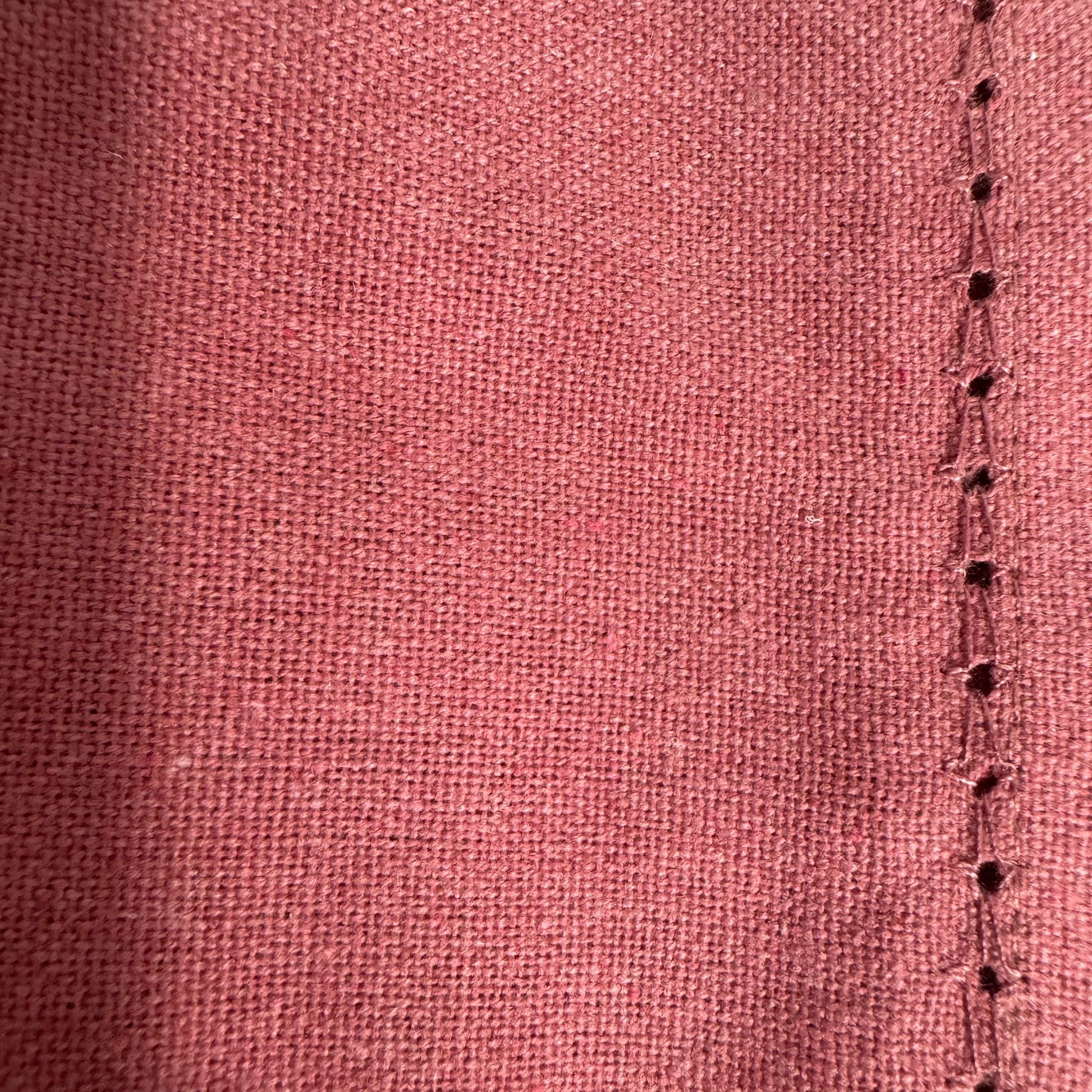 Close-up image of a burgundy cotton fabric showcasing its texture with a neat stitched edge, highlighting the fine details and craftsmanship