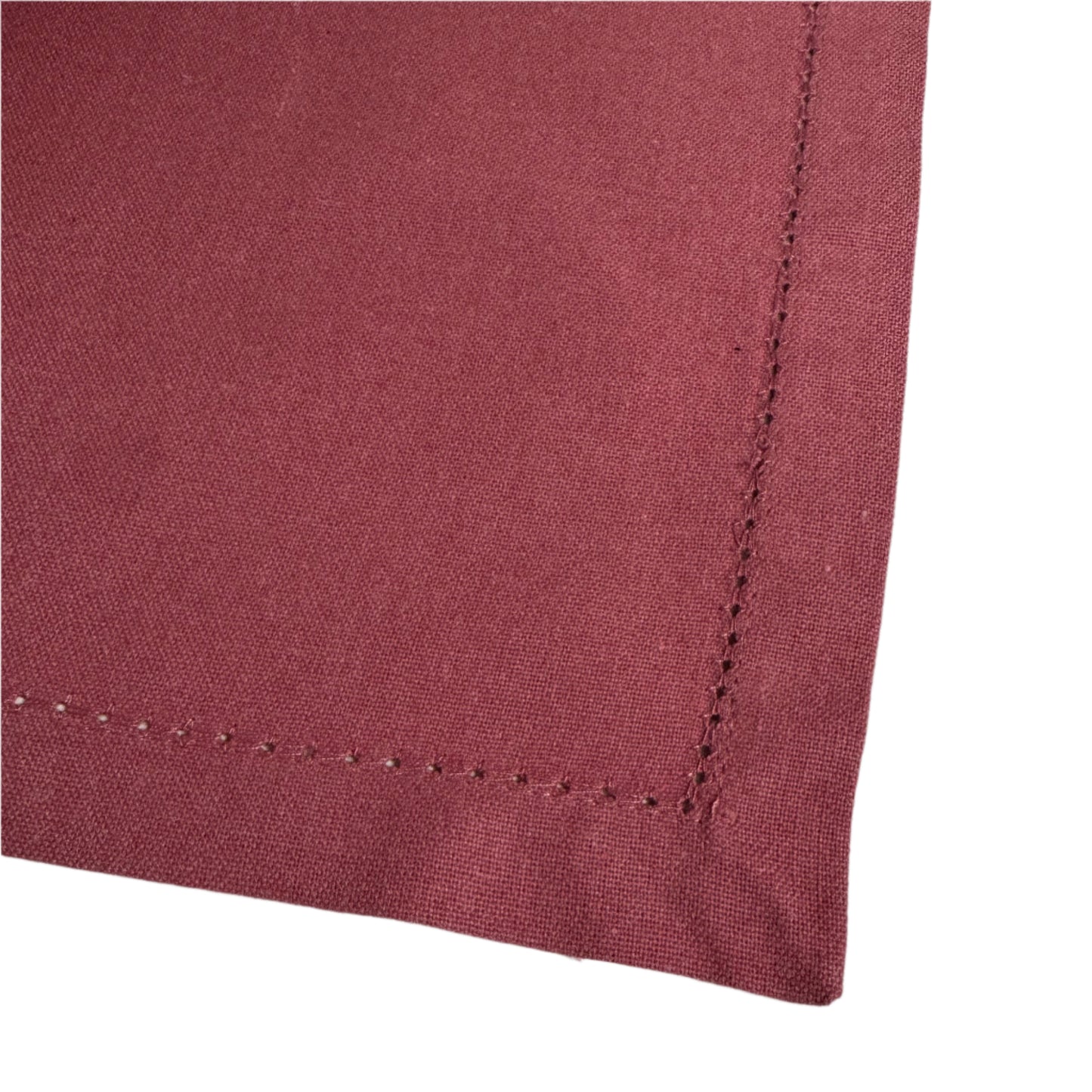 Close-up of a corner of a burgundy cotton napkin, featuring a neatly stitched edge