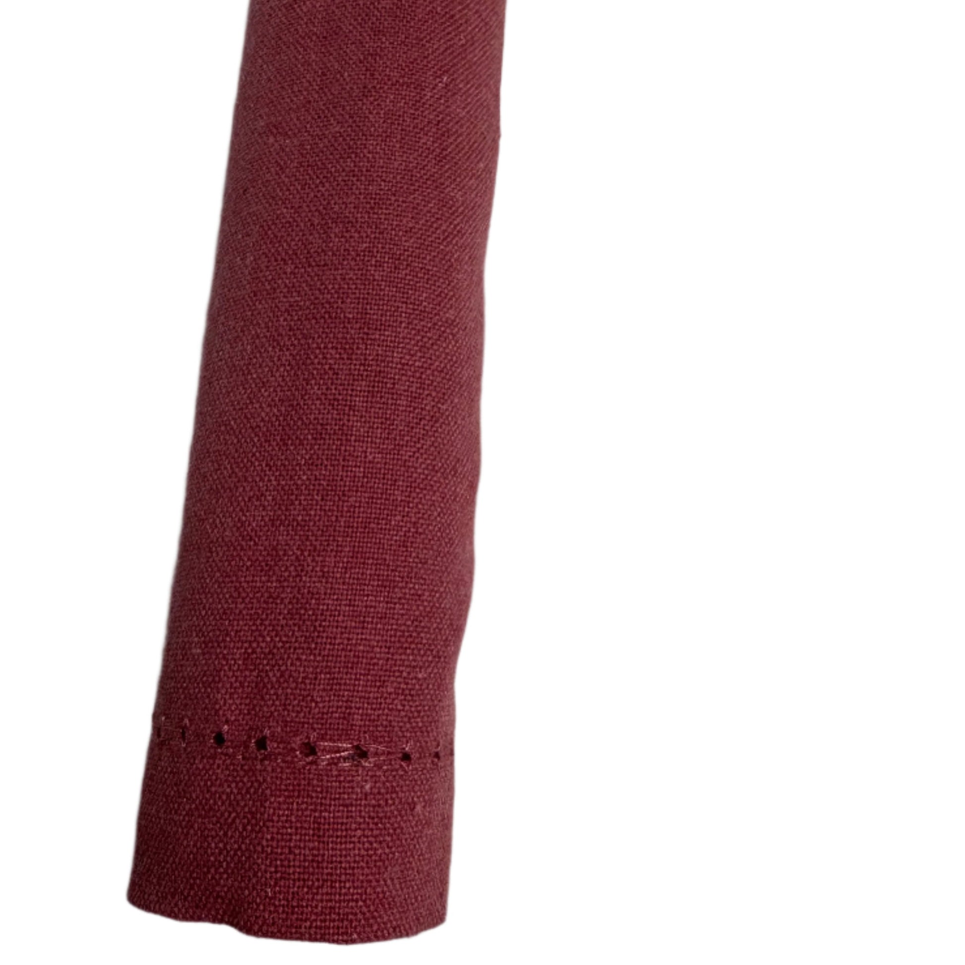 Close-up of a neatly rolled cotton napkin in a burgundy color, highlighting the delicate stitching along the edge