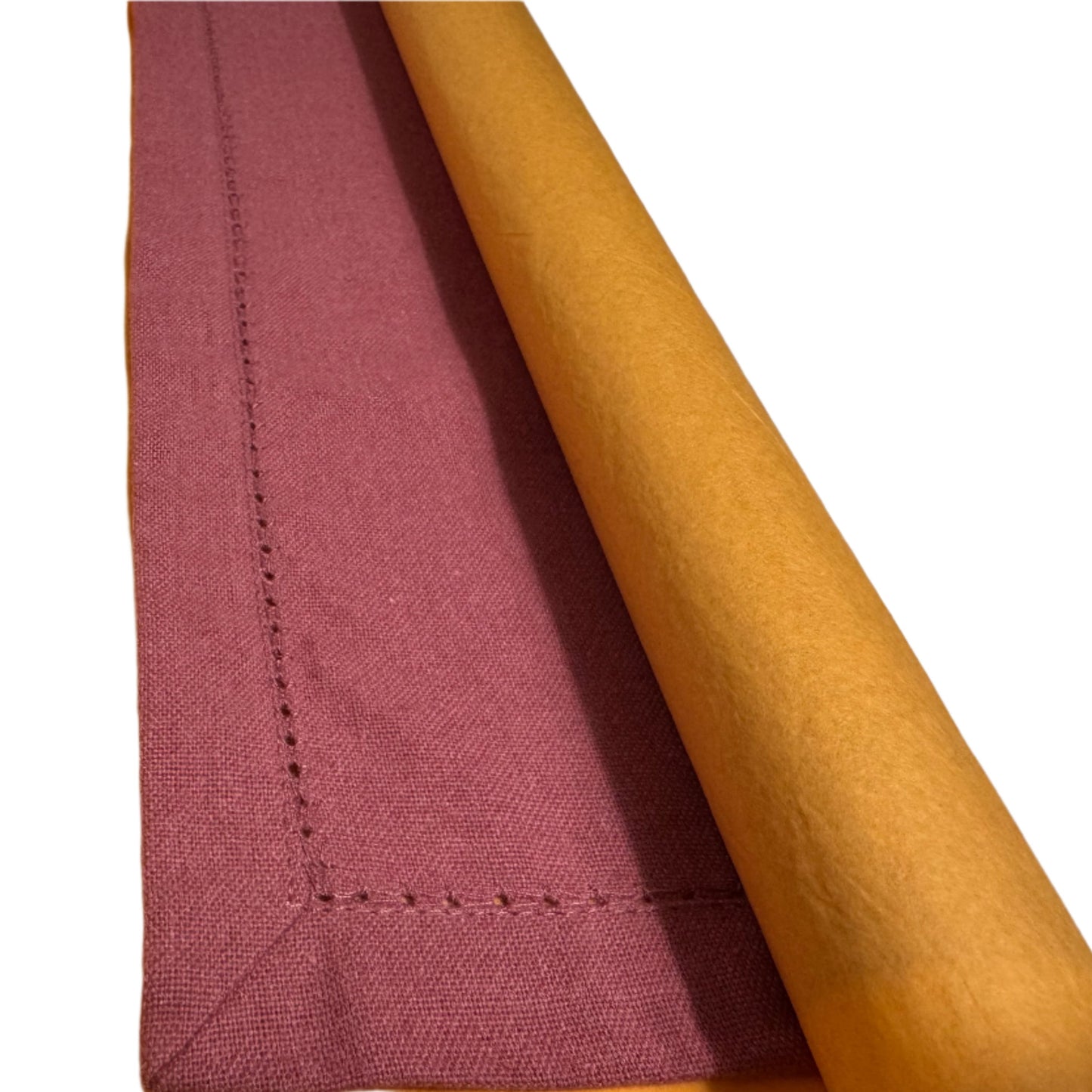 A rolled cotton napkin in a rich rose color, paired with a mustard yellow paper wrapping, showing the neat folding and hemstitch detail along the edges