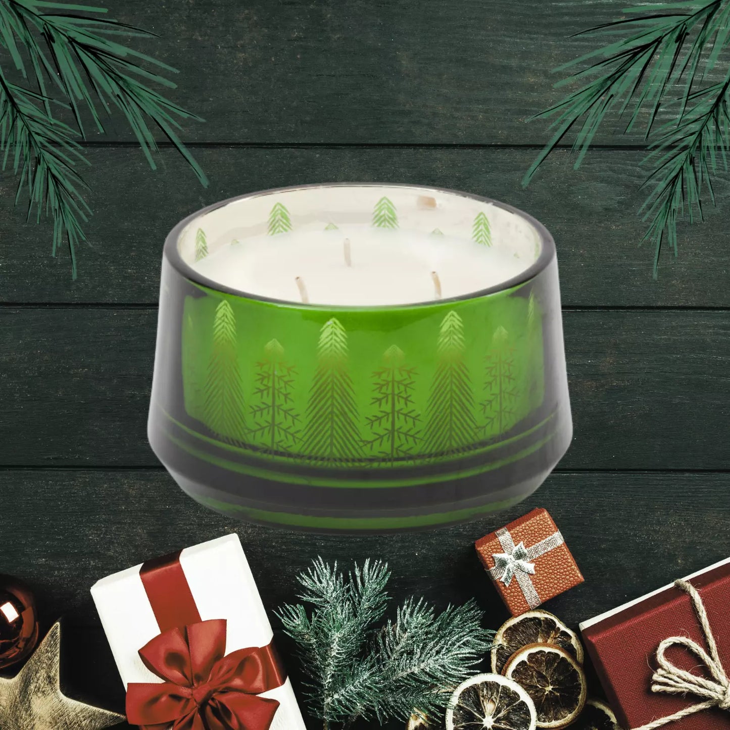 An 18oz Pine and Sage 3-Wick Candle with a Christmas tree motif, hand-poured, displayed in a green glass container surrounded by festive decorations including Christmas trees and wrapped gifts.