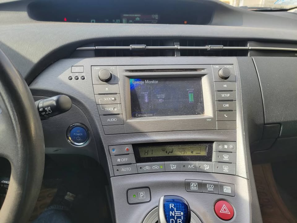Close-up of the center console and infotainment system in a Toyota Prius, showing the energy monitor display, climate controls, gear selector, and EV driving modes.