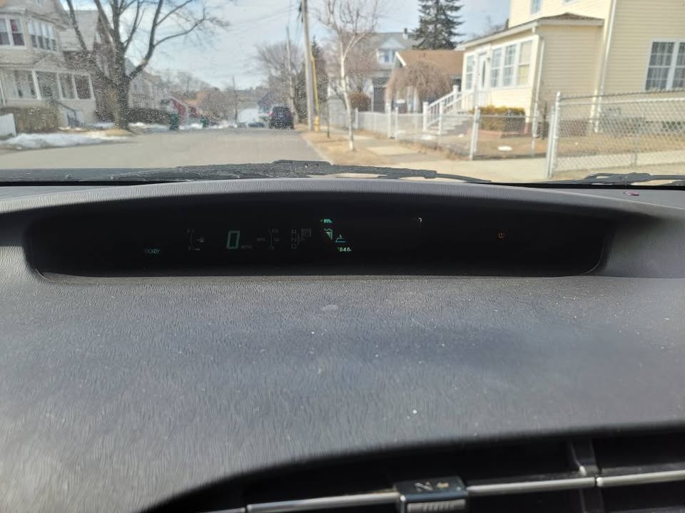 Dashboard view from a 2013 Toyota Prius showing 0 MPH and 195,846 miles on the odometer with a residential street in the background.