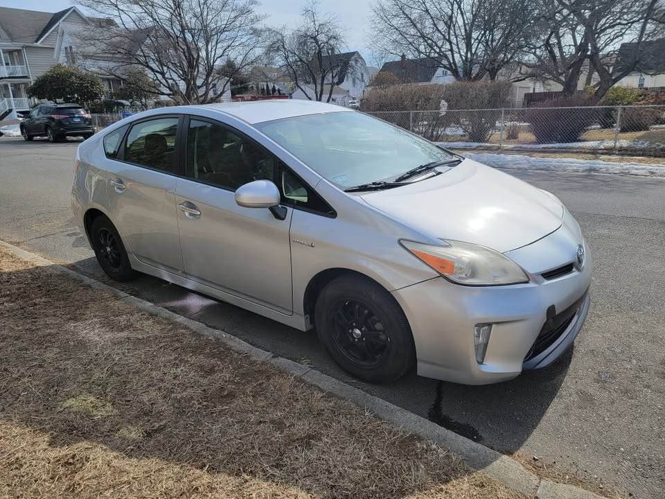 Driver-side front angle view of a silver 2013 Toyota Prius parked curbside on a residential street, showing clean body with black steel wheels