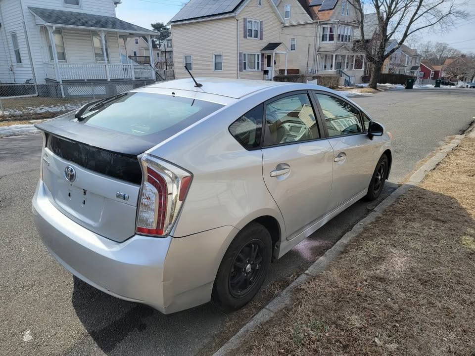 Rear and passenger-side view of a silver 2013 Toyota Prius parked on a residential street, showing the black trunk panel and black steel wheels.