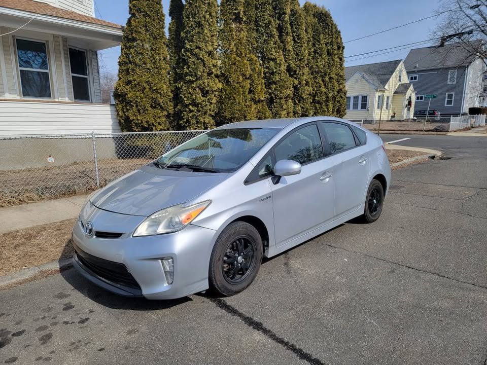 Front passenger-side view of a silver 2013 Toyota Prius parked on a residential street, showing clean body panels, black steel wheels, and hybrid badge.