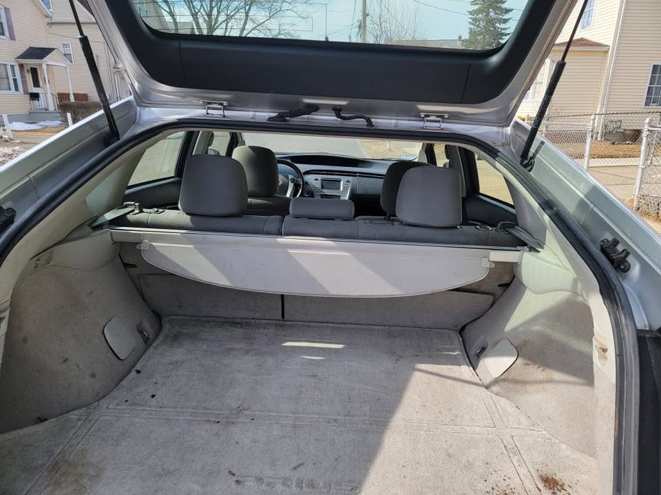 Interior view of the open trunk of a 2013 Toyota Prius, showing spacious cargo area with light gray carpeting, a retractable cargo cover, and folded rear seats.