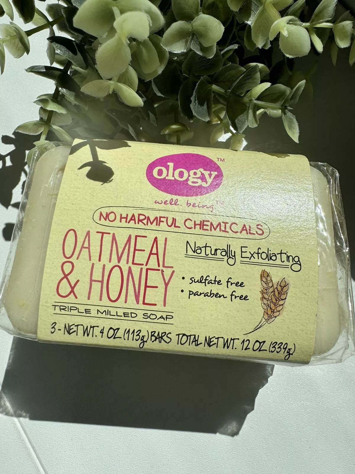 Pack of Ology oatmeal and honey triple milled soap bars, naturally exfoliating and sulfate-free, placed near greenery in natural light