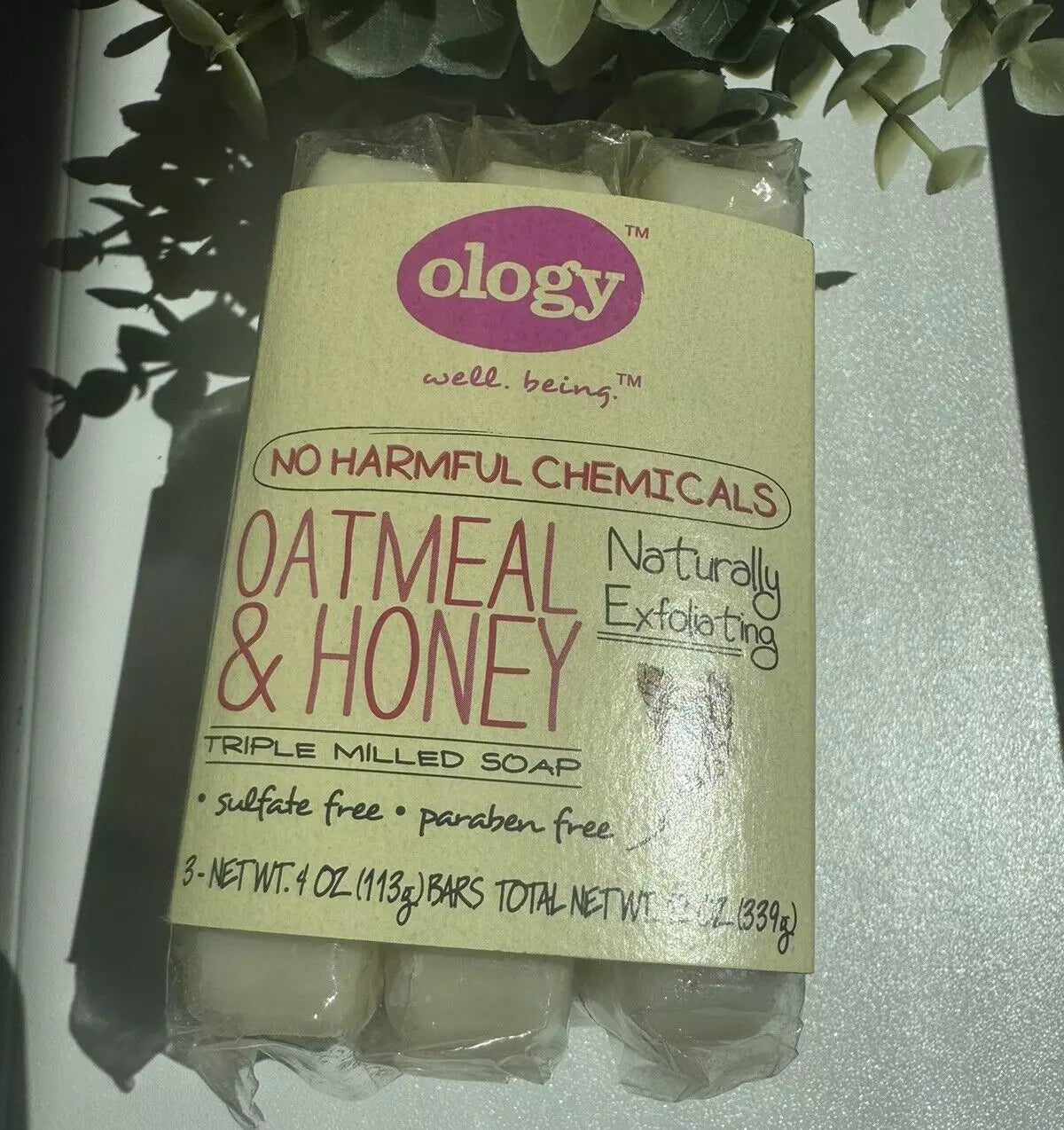 Ology oatmeal & honey triple milled soap 3-pack on white surface, labeled sulfate-free, paraben-free, and naturally exfoliating, shown with plant leaves overhead