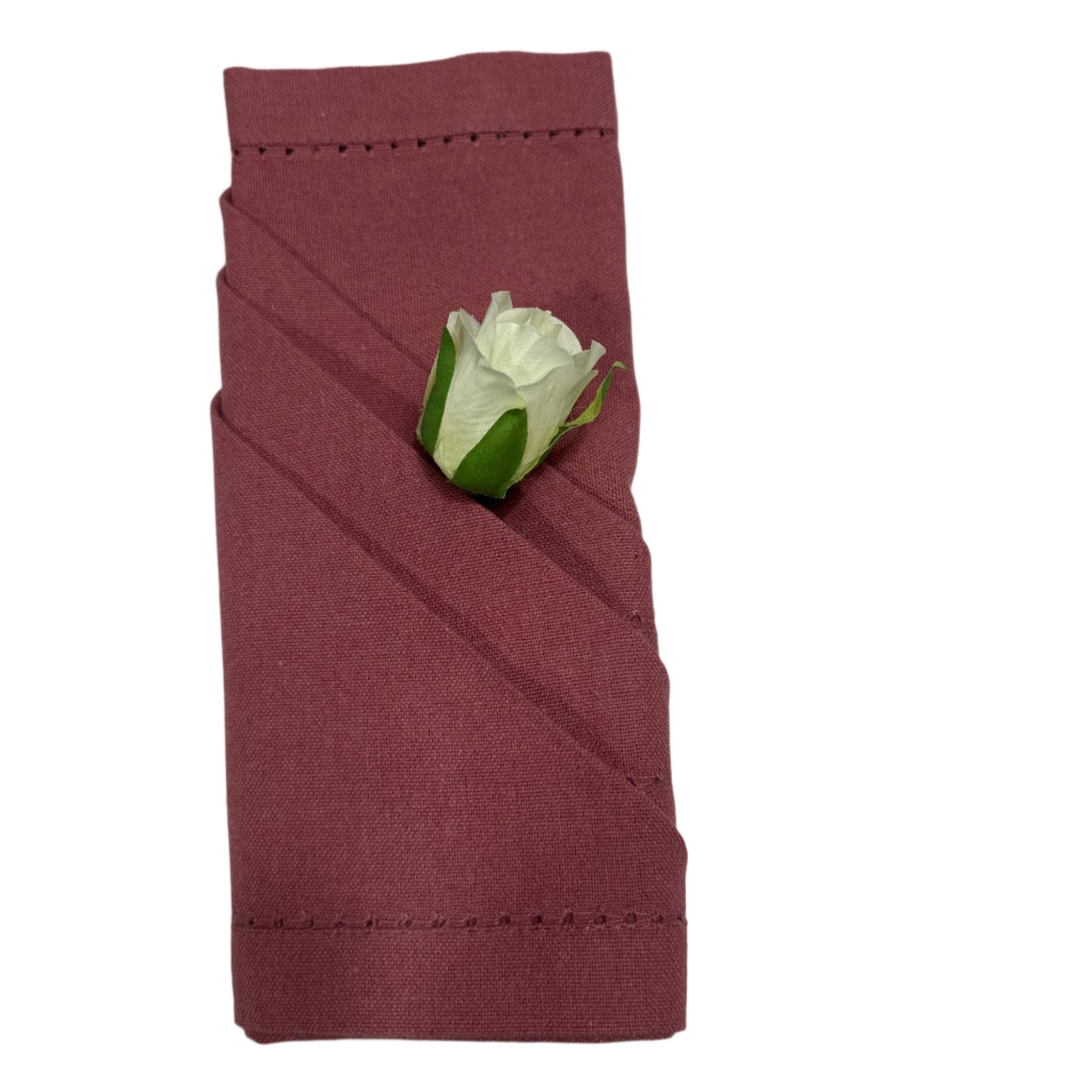 A folded cotton napkin in a warm rose color with a diagonal fold and a small artificial white rose accent on top, featuring delicate hemstitching along the edges