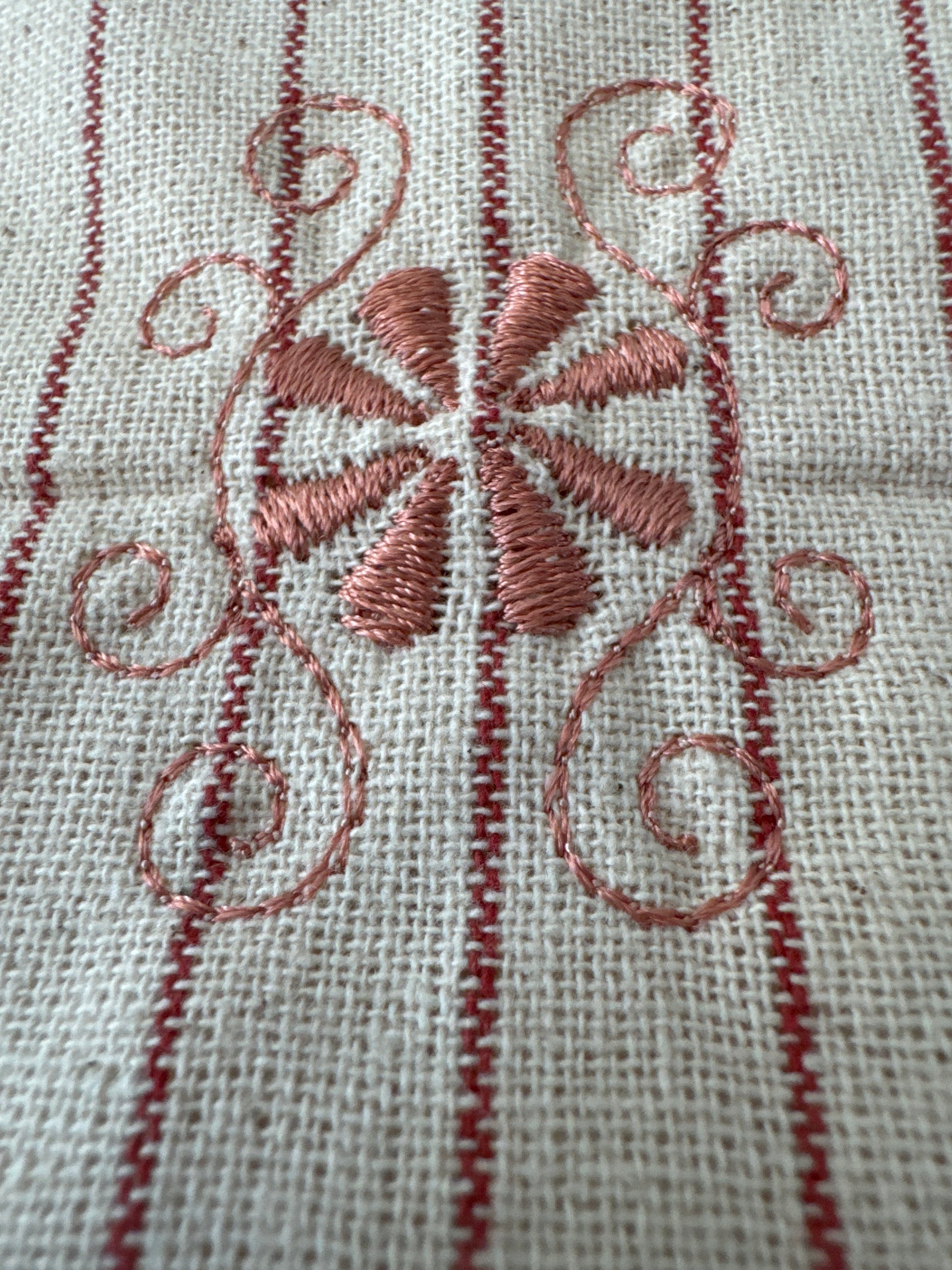 Unbleached cotton cloth napkin with delicate red embroidered floral motif and fine stripe detailing, 12 x 12 inch reusable eco friendly table napkin shown folded on a neutral background