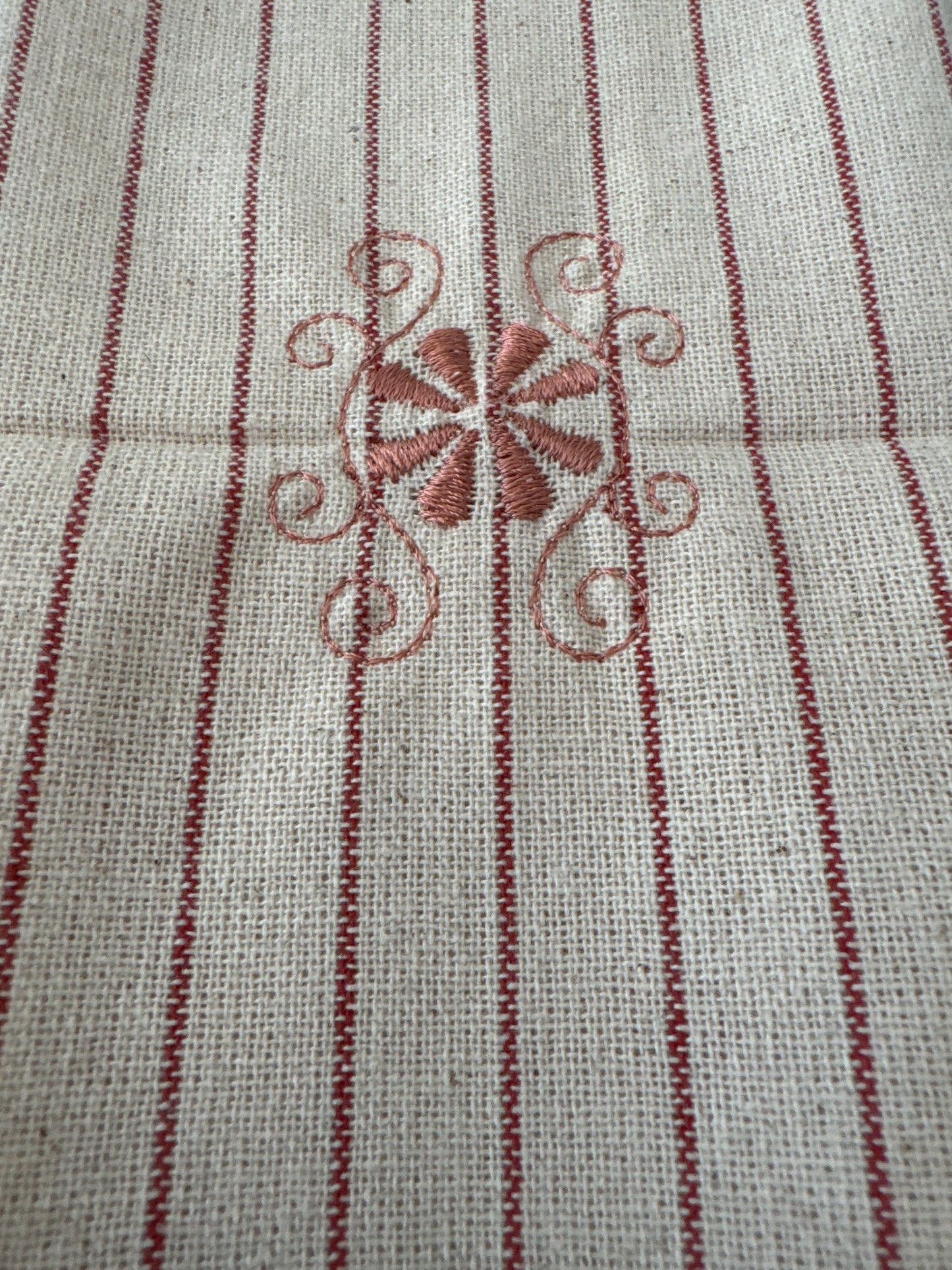 Unbleached cotton cloth napkin with delicate red embroidered floral motif and fine stripe detailing, 12 x 12 inch reusable eco friendly table napkin shown folded on a neutral background