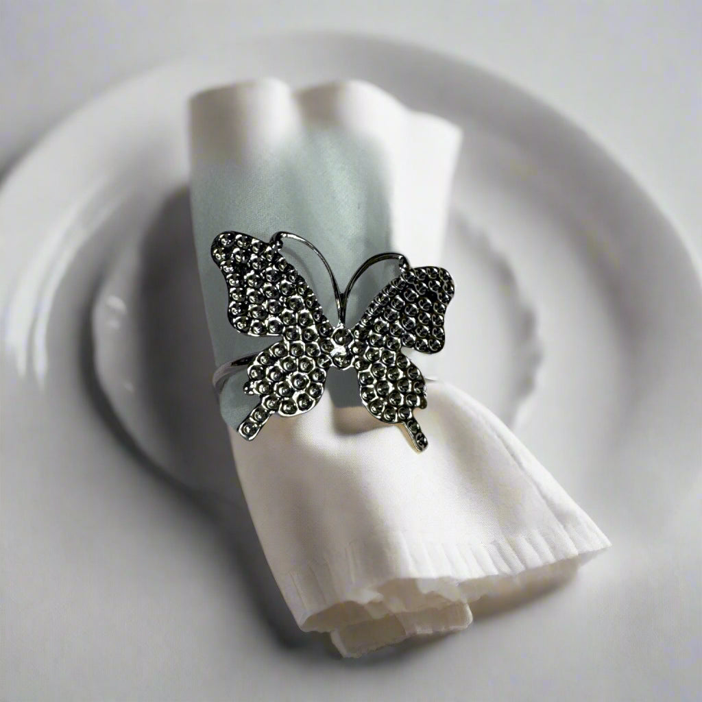 Set of 6 silver butterfly napkin rings displayed on cloth napkin and dish.

